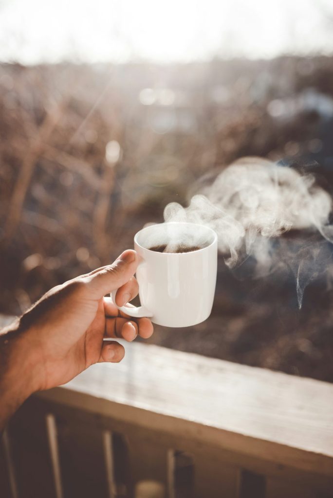 On porch holding steaming coffee cup